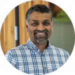 A headshot of Sumeet Mahajan wearing a blue check shirt and smiling at the camera.